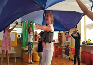 dzieci unoszą wysokochustę tworząc parasol a dziewczynka przebiega pod nią na druga stronę koła